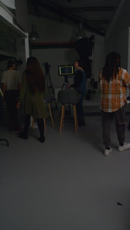 Vertical-Video-Of-Actors-Meeting-Female-Film-Director-And-Crew-On-Film-Set-Shooting-Movie-Or-Video-In-Studio